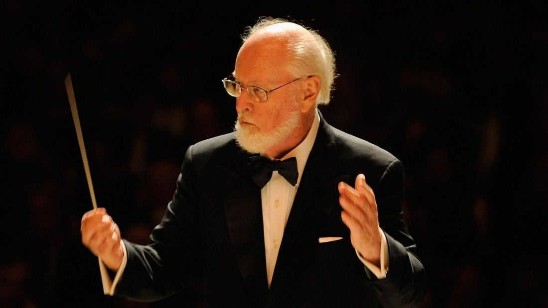 John Williams en smoking, lunettes et barbe blanche, baguette levée, dirige un orchestre