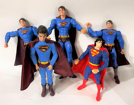 Plusieurs figurines Superman articulées alignées, dans différentes tailles et versions du costume